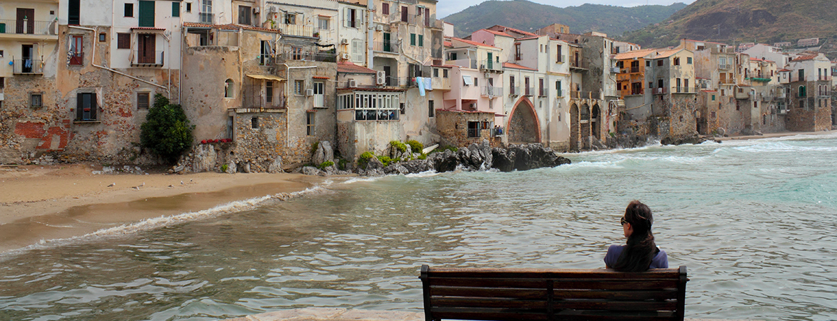 Woman sitting on bench along the shore in Cefalu