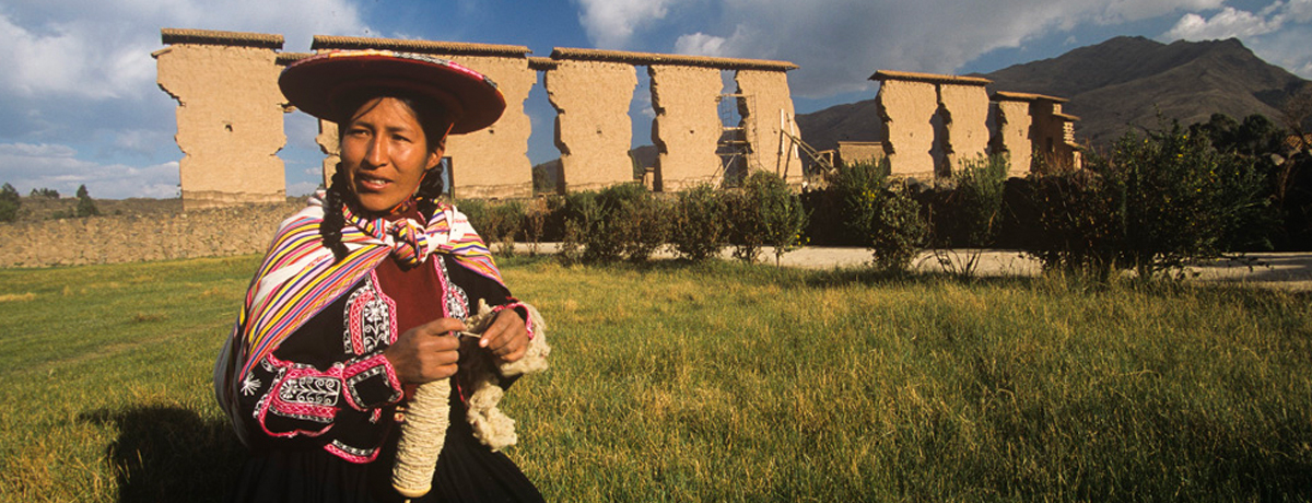 Peruvian woman sitting in the grass winding yarn around a spool