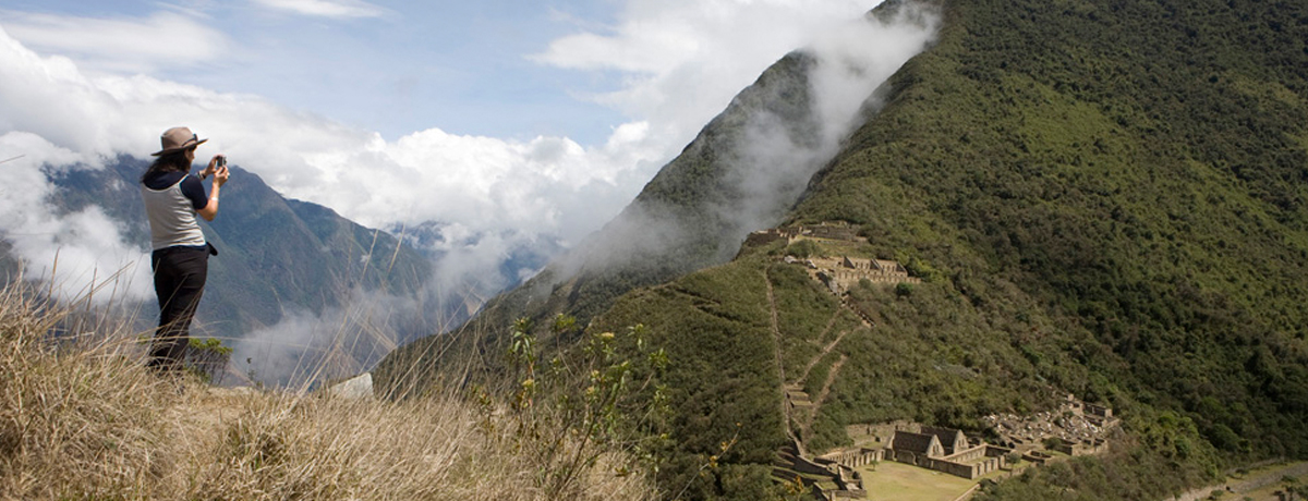 Individual high atop a cliff photographing Machu Picchu