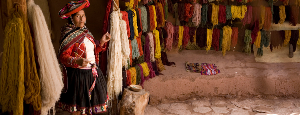 Peruvian woman beside wall of colorful yarn