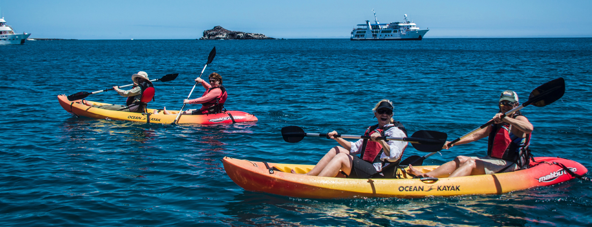 Two kayakers paddle through water with Isabela II in the background