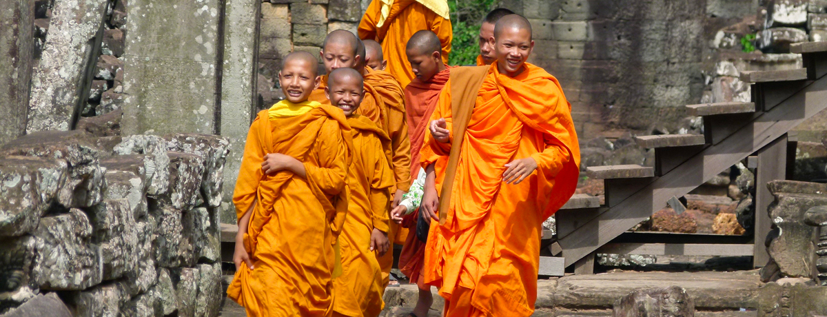 Young locals dressed in orange robes walking from a Cambodian temple