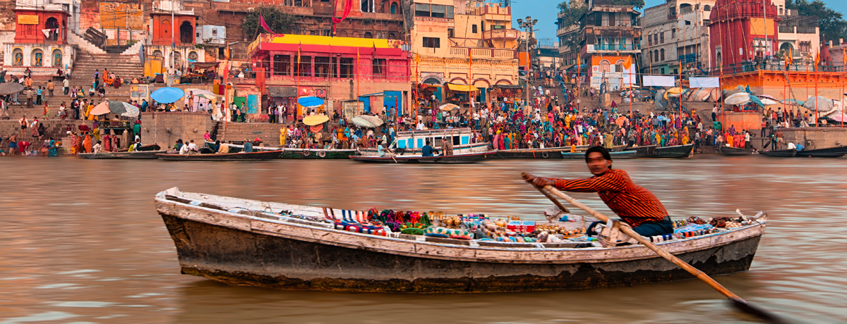 Boatman rowing through water with holy ghats of Varanasi in background