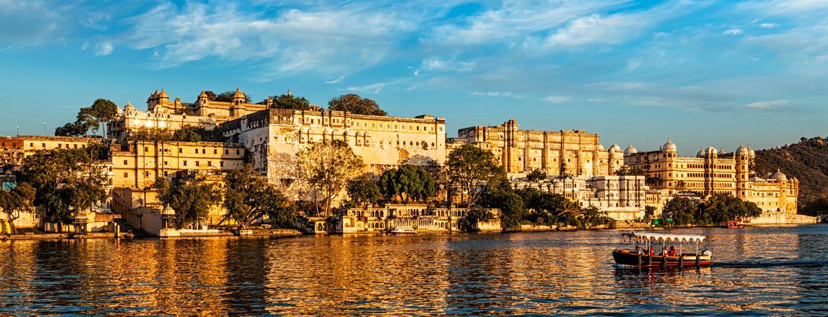 City Palace in Udaipur with tourist boat on Lake Pichola at sunset