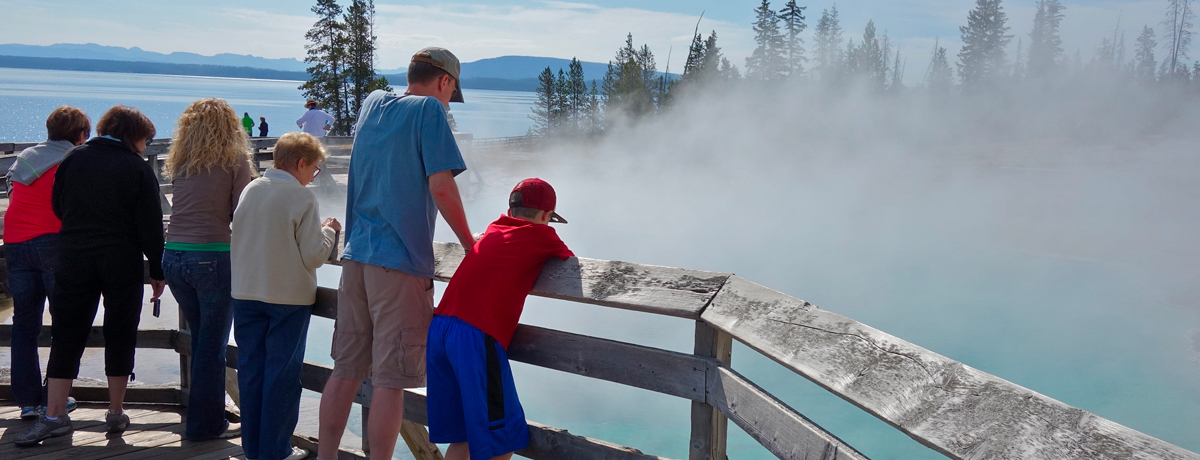 Guests perched on a boardwalk watching Old Faithful erupt