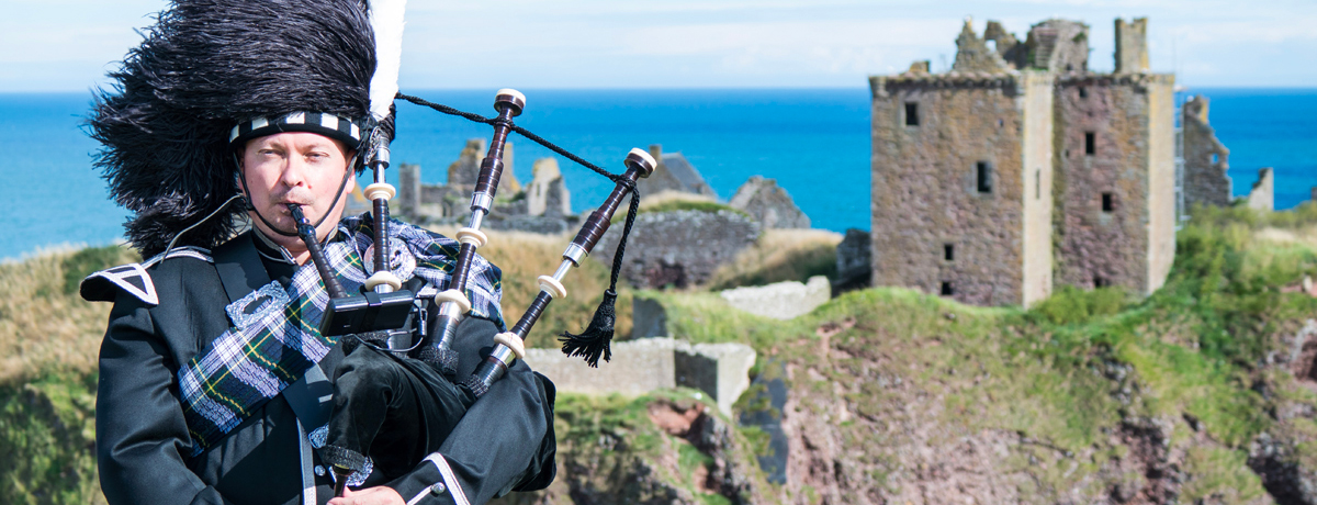 Traditional Scottish bagpiper in full dress code in front of Dunnottar Castle 