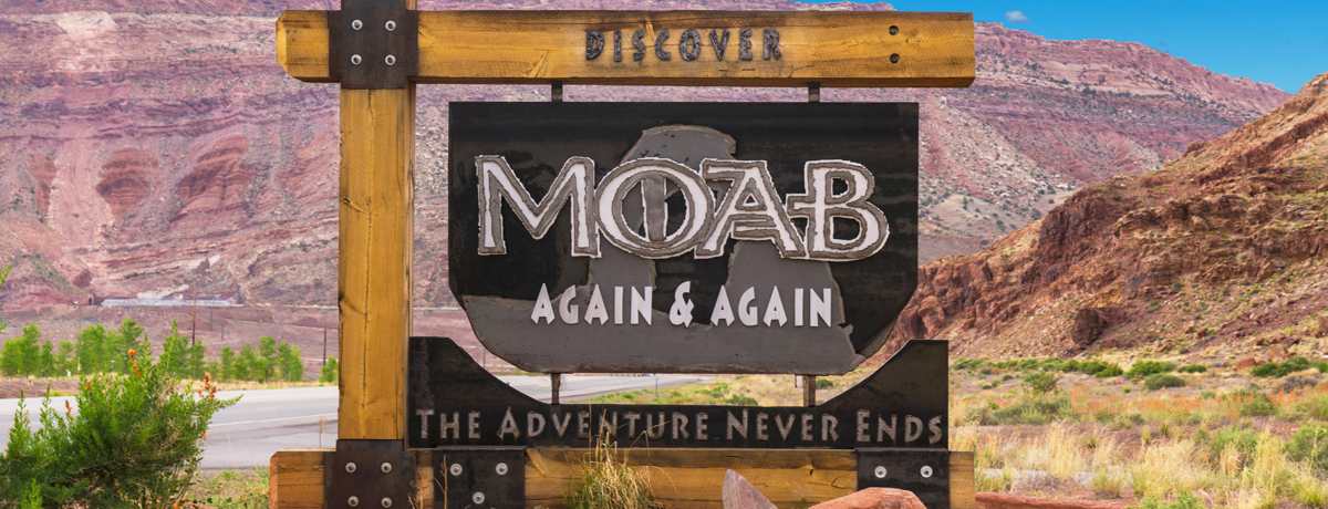 Sign for town of Moab that reads Moab Again & Again The Adventure Never Ends